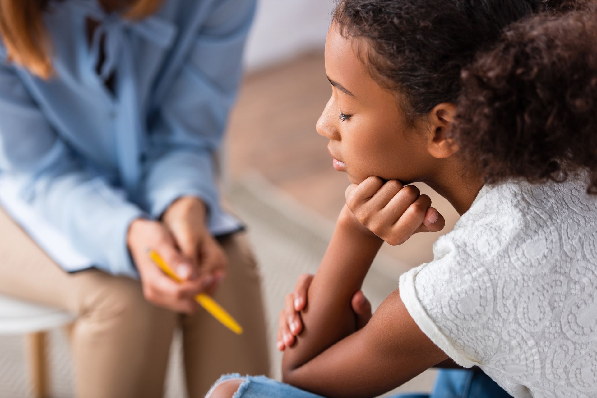 A little girl is sitting on the floor talking to a female therapist.