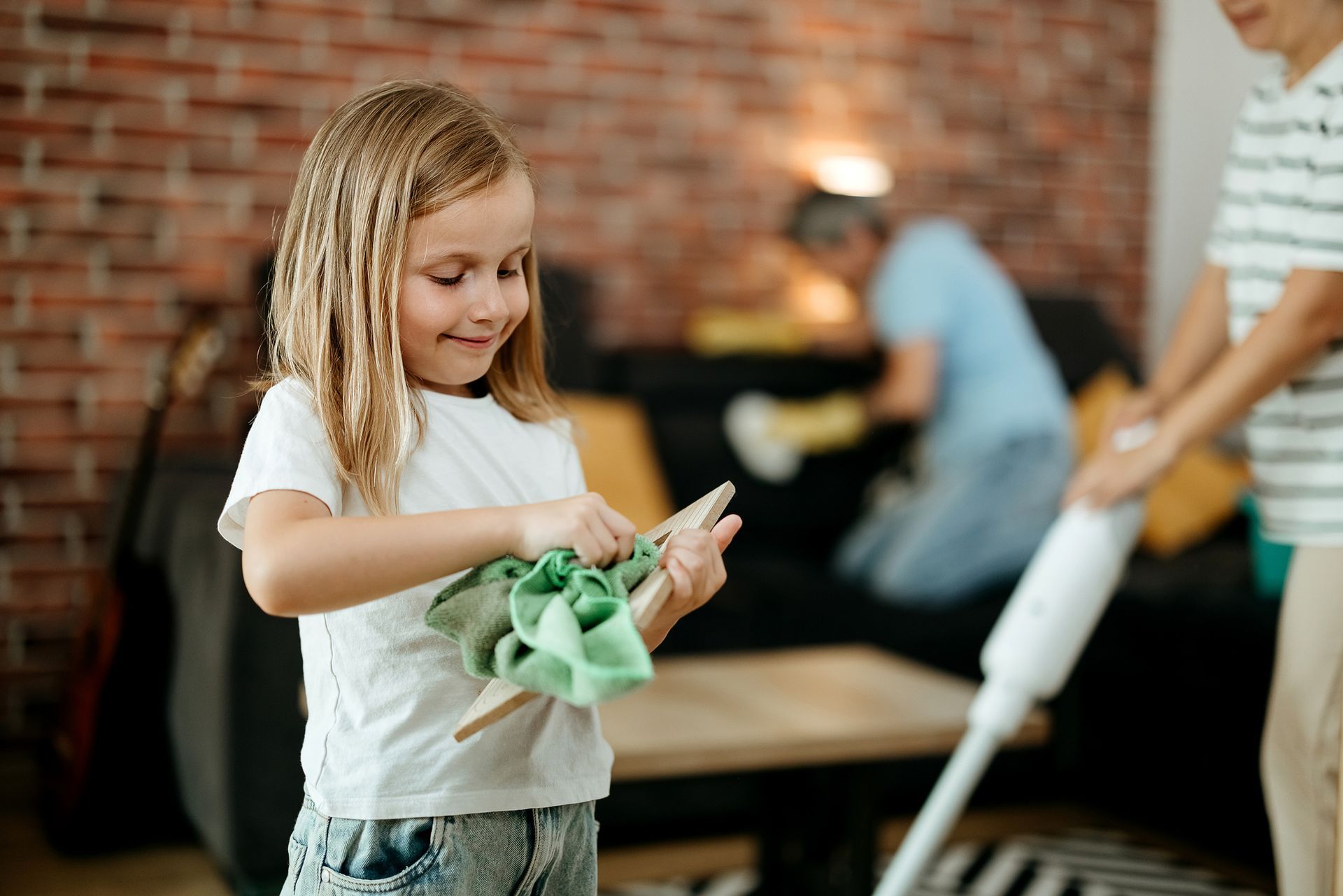 A little girl is cleaning a table with a cloth in a living room.