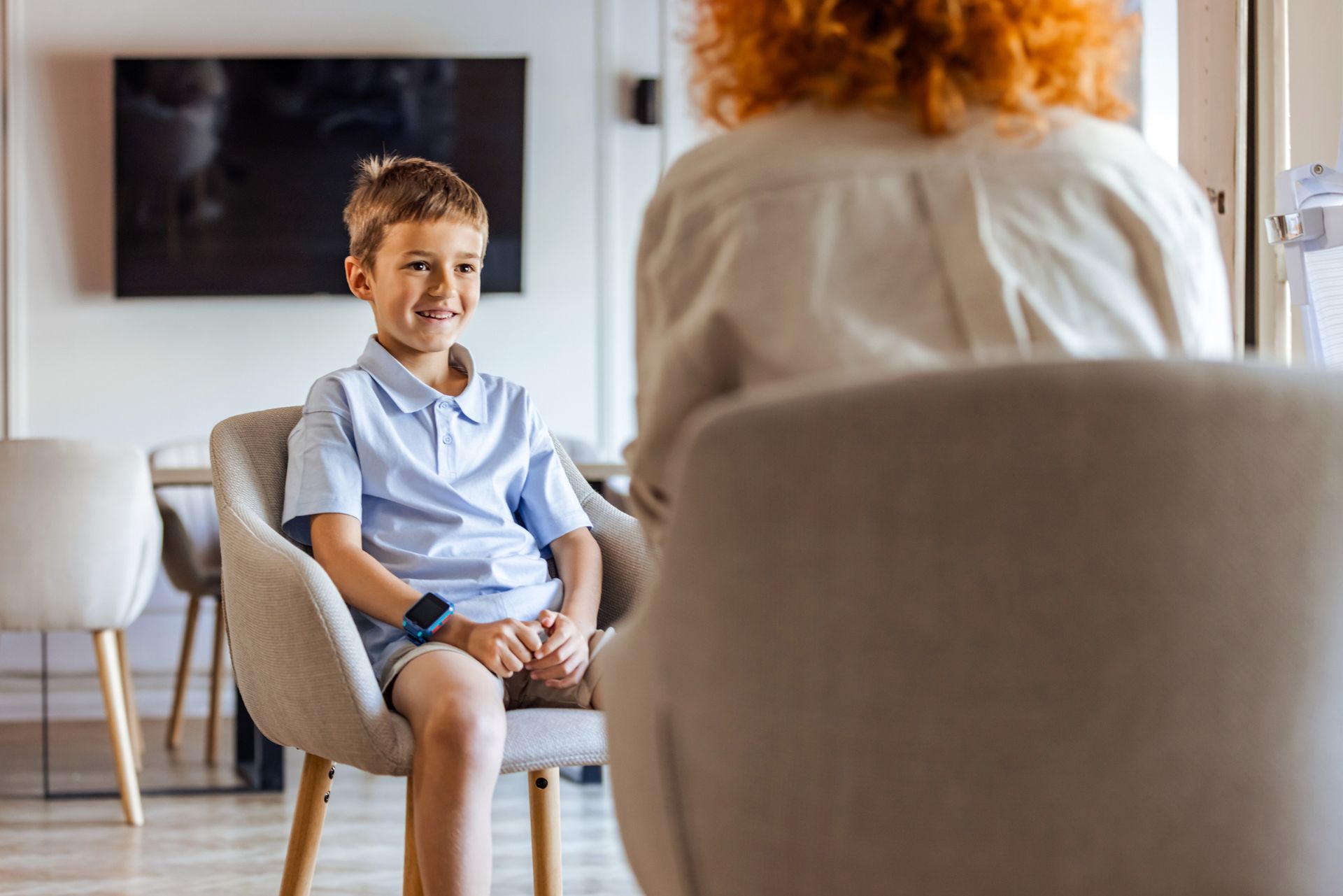 A young boy is sitting in a chair talking to a woman.