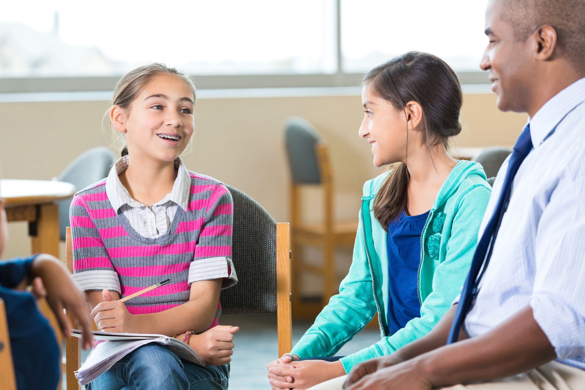 A man and two girls are sitting in chairs talking to each other.