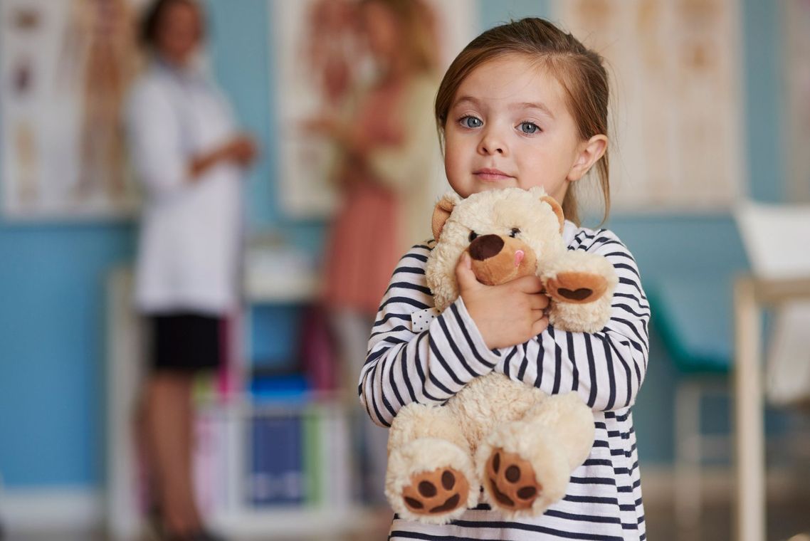 A little girl is holding a teddy bear in a doctor 's office.