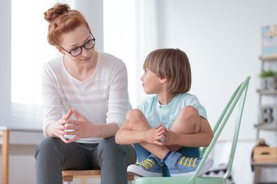 A woman is sitting on a chair talking to a young boy.