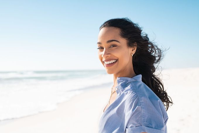 A woman is smiling on the beach and looking at the camera.