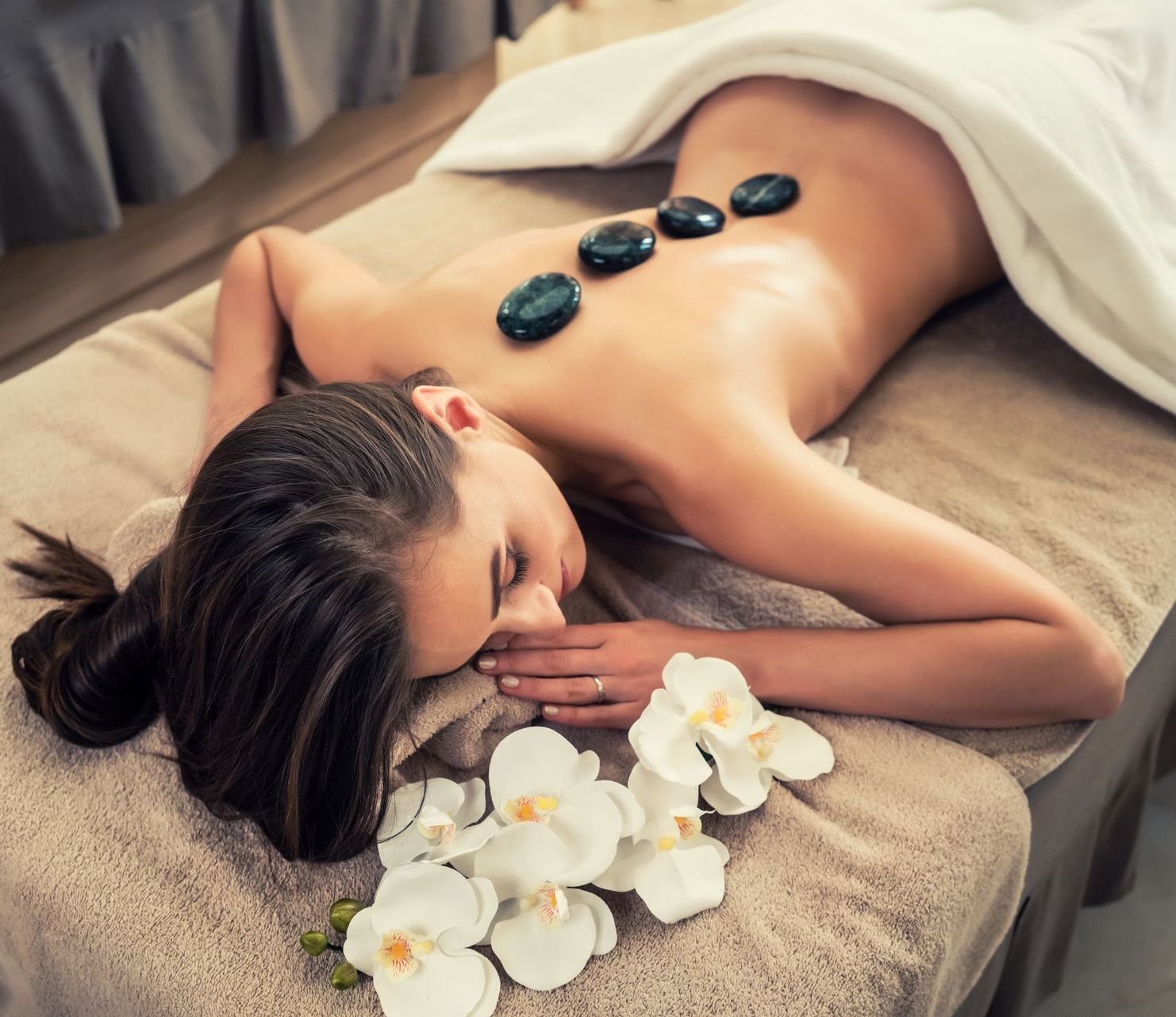 A woman is laying on a bed with rocks on her back.