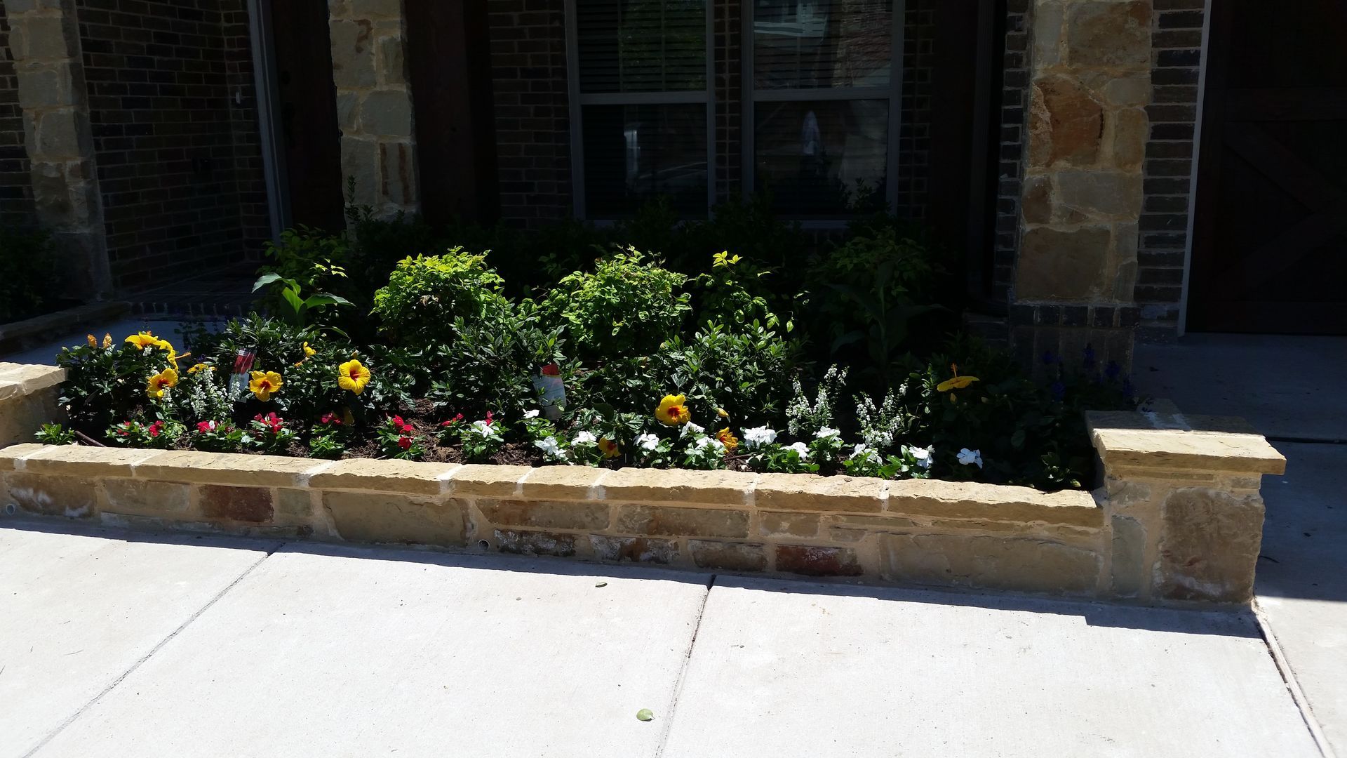 A stone planter filled with flowers in front of a house.