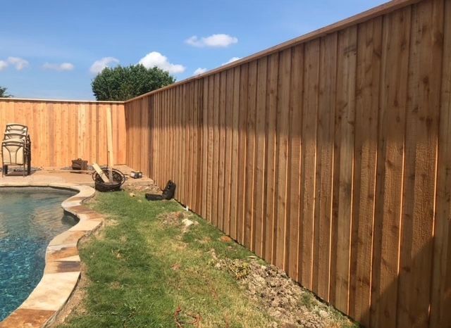 A wooden fence surrounds a swimming pool in a backyard.