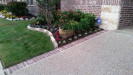 A brick walkway leading to a house with flowers and a mailbox.