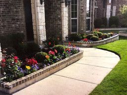 A brick house with a sidewalk and flowers in front of it.