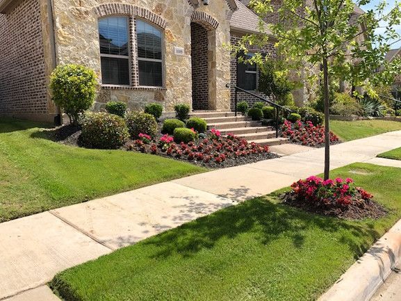 A house with a lush green lawn and flowers in front of it.