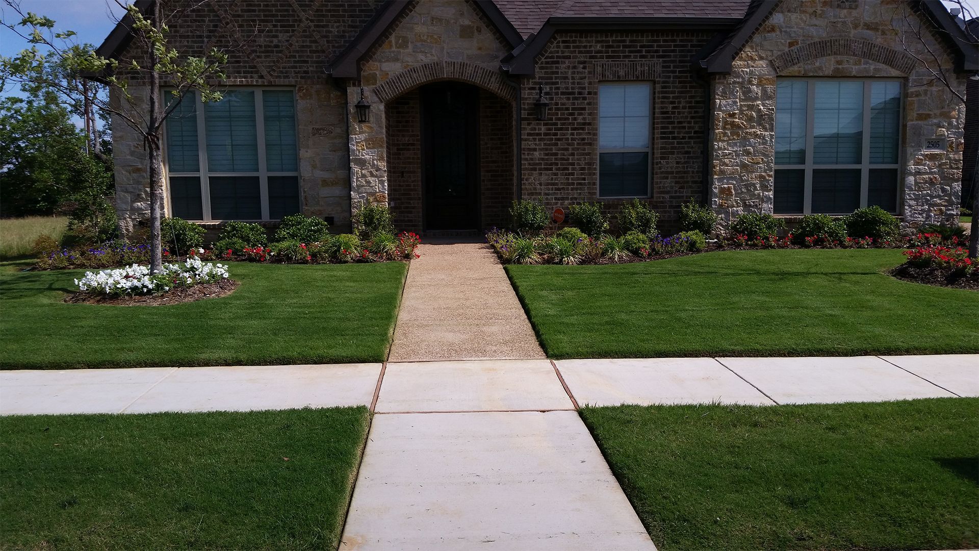 A brick planter filled with pink flowers in front of a brick house.