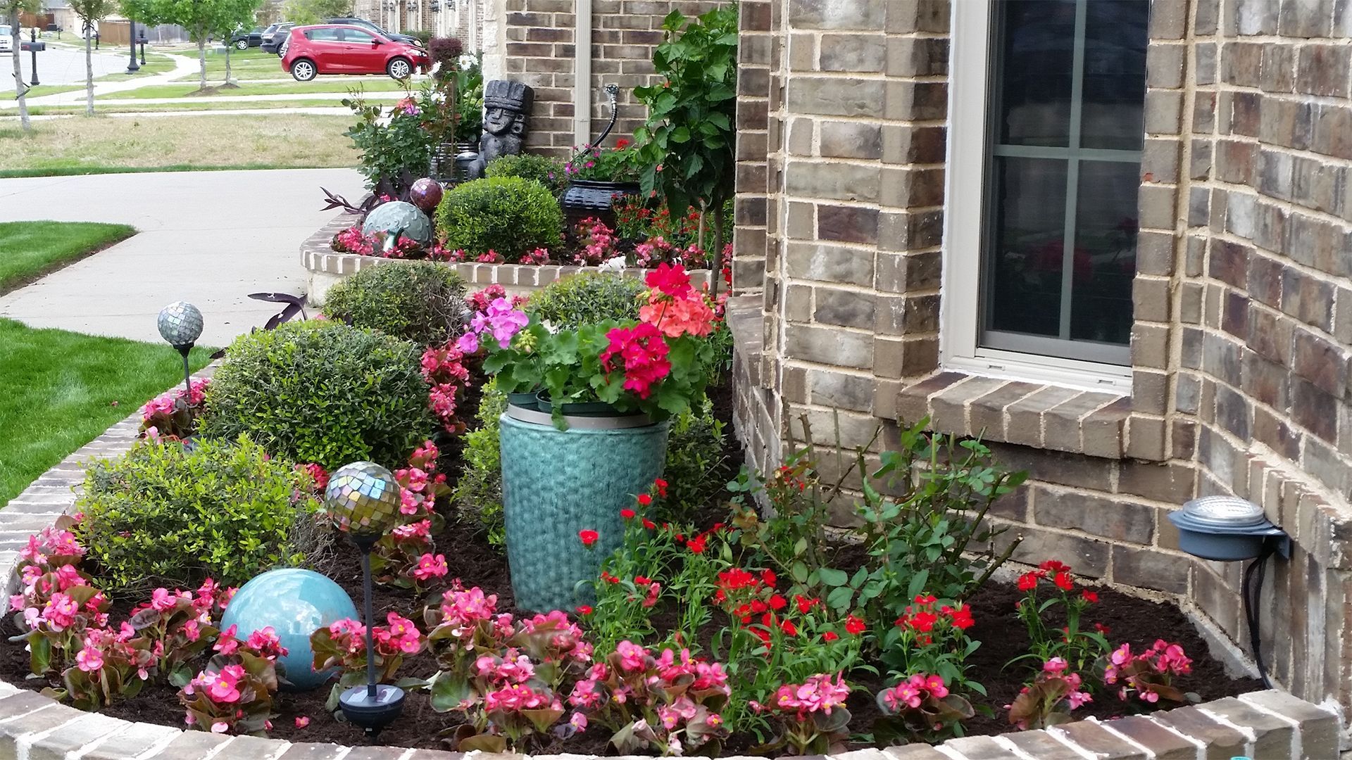 Colorful flower bed with pink blooms and decorative pots beside a brick house and window