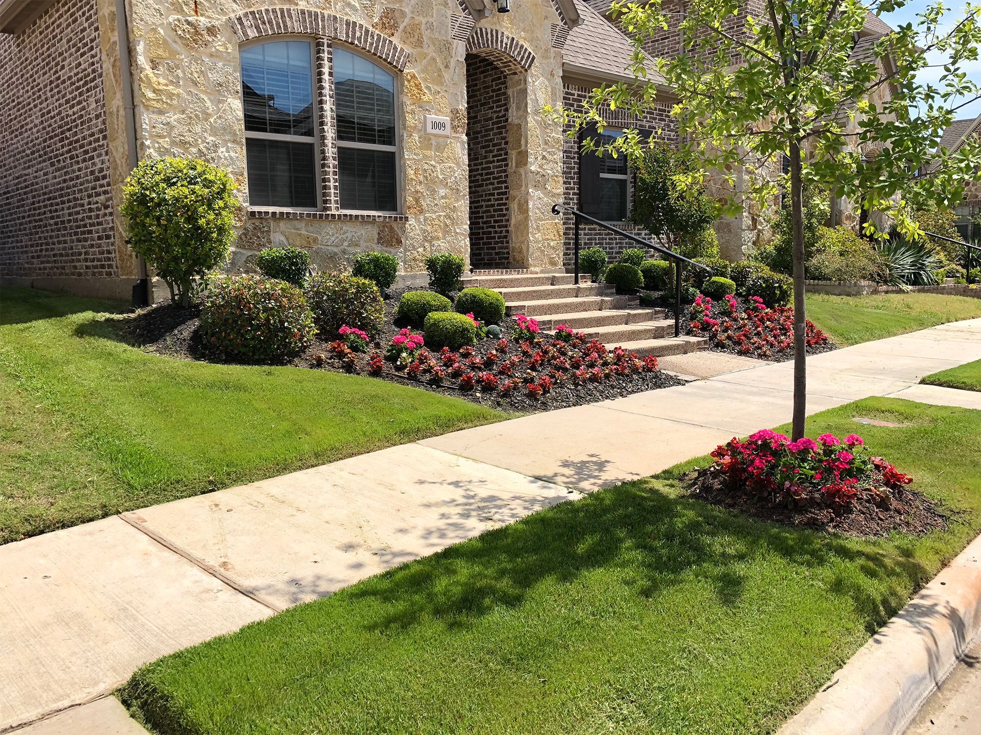 A brick planter filled with pink flowers in front of a brick house.