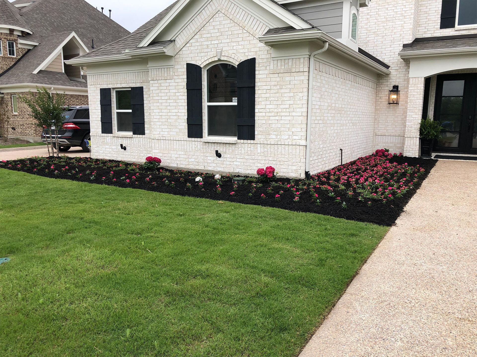A sidewalk with a bed of flowers in front of a house.
