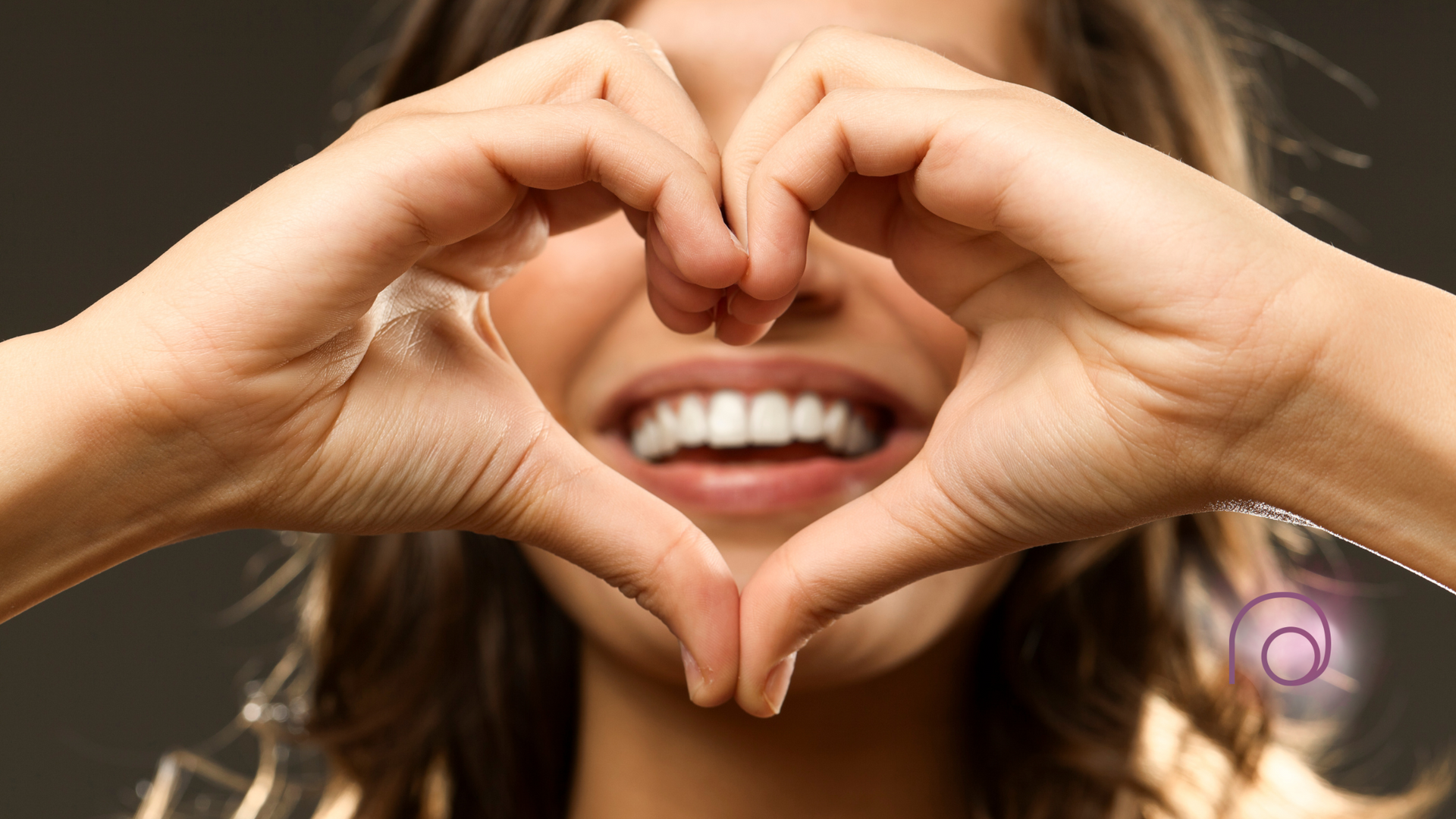 A woman is making a heart shape with her hands in front of her face.