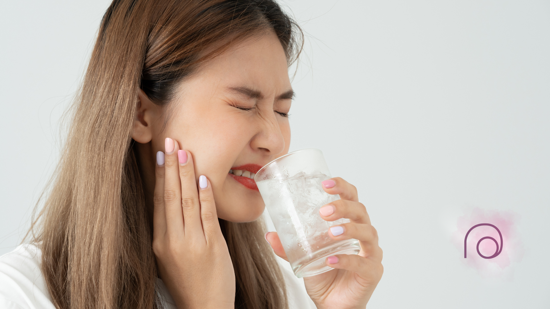A woman is holding her face in pain while drinking a glass of water.