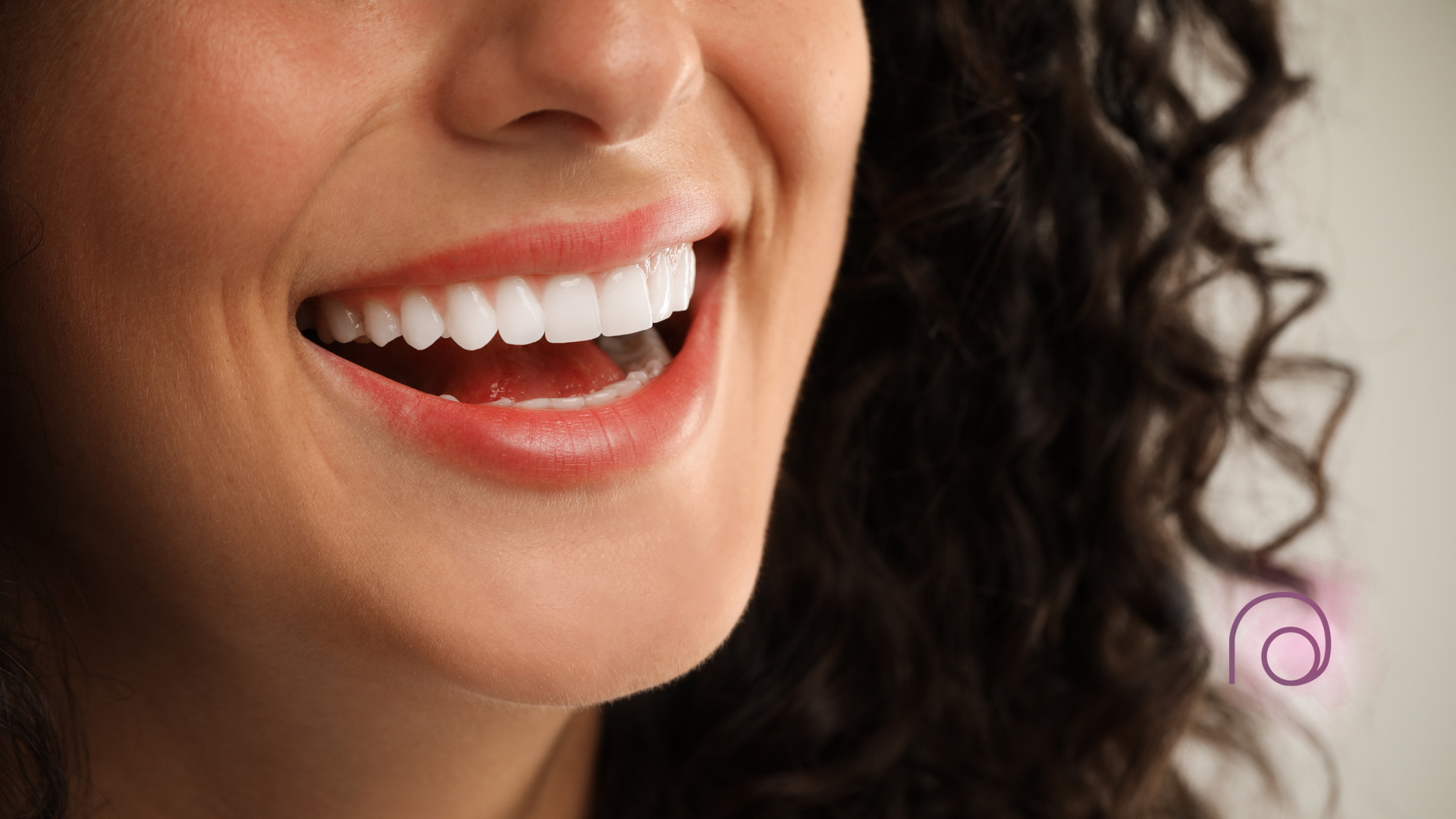 A woman with curly hair is smiling with her mouth open and her teeth showing.