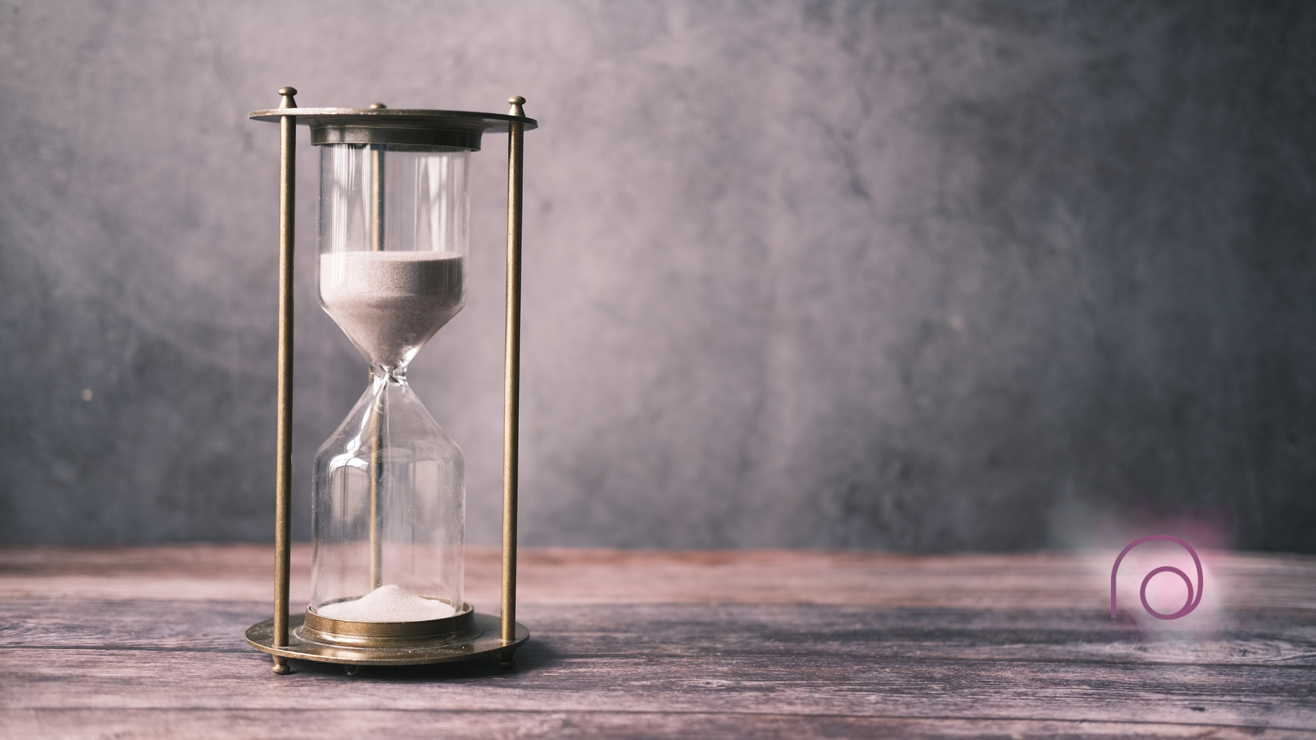 Hourglass on a wooden surface, grains of sand falling, against a muted background.