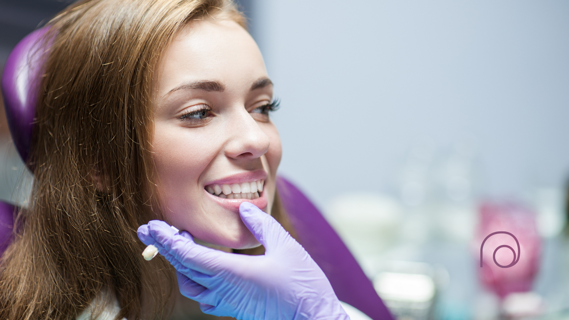 A woman is sitting in a dental chair while a dentist examines her teeth.