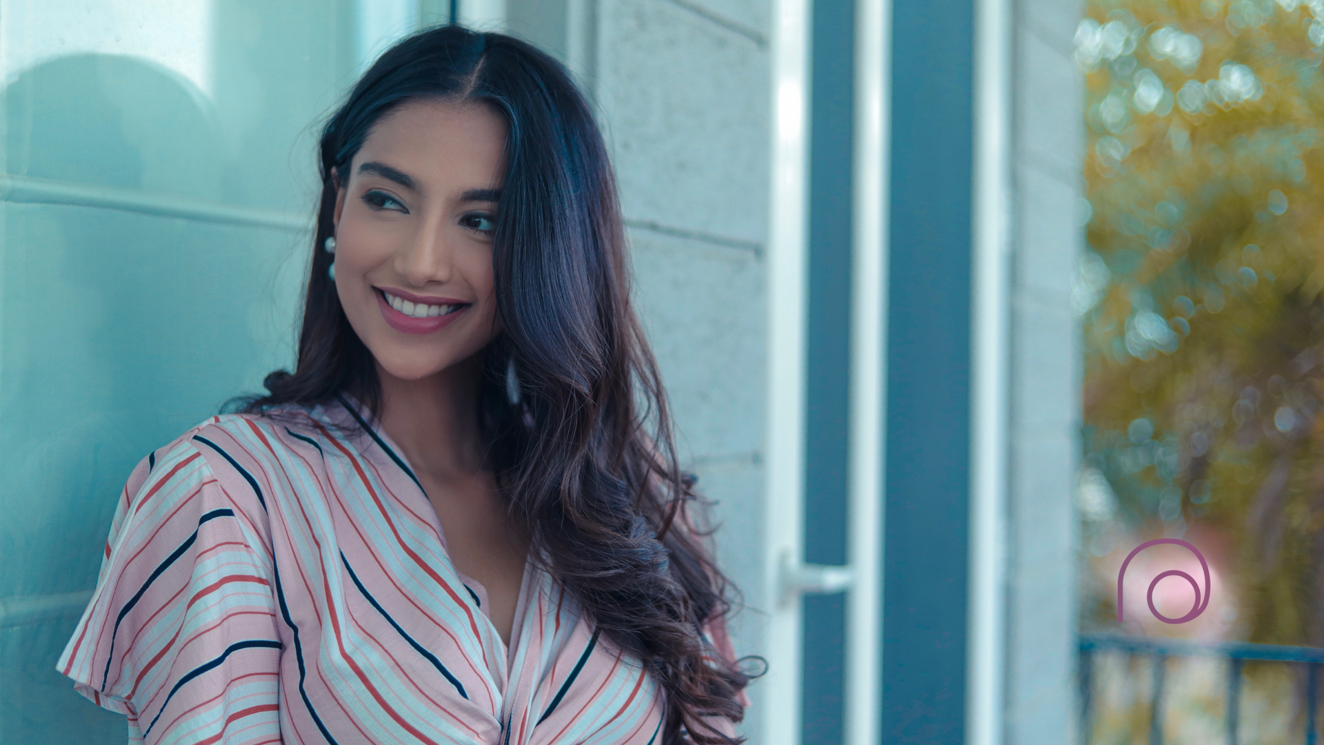 A woman in a striped shirt is smiling while standing in front of a door.