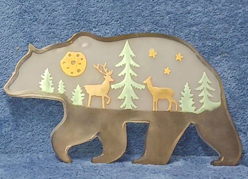 A resin silhouette of a bear with trees and deer on it