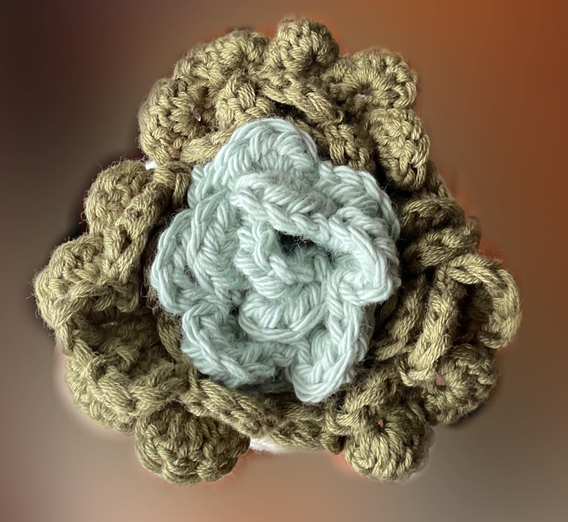 A close up of a crocheted flower on a brown background