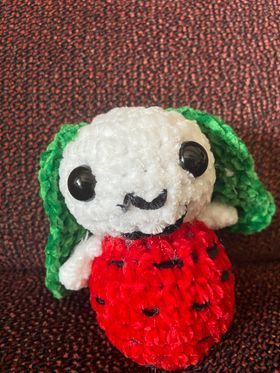 A stuffed hand crocheted bunny with green ears holding a strawberry is sitting on a couch.