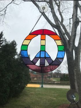 A stained glass peace sign is hanging in a window