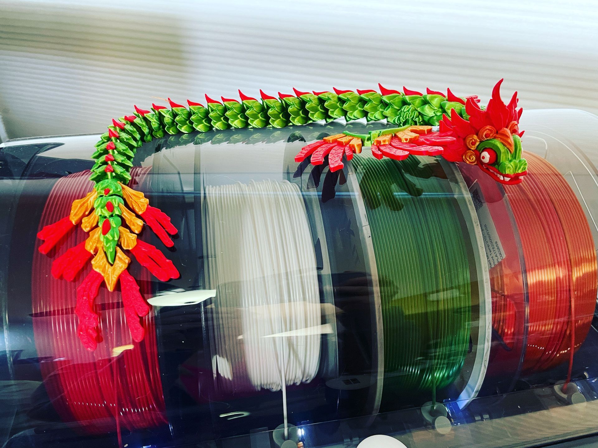 A toy dragon is sitting on top of a spool of 3d Printing colorful plastic