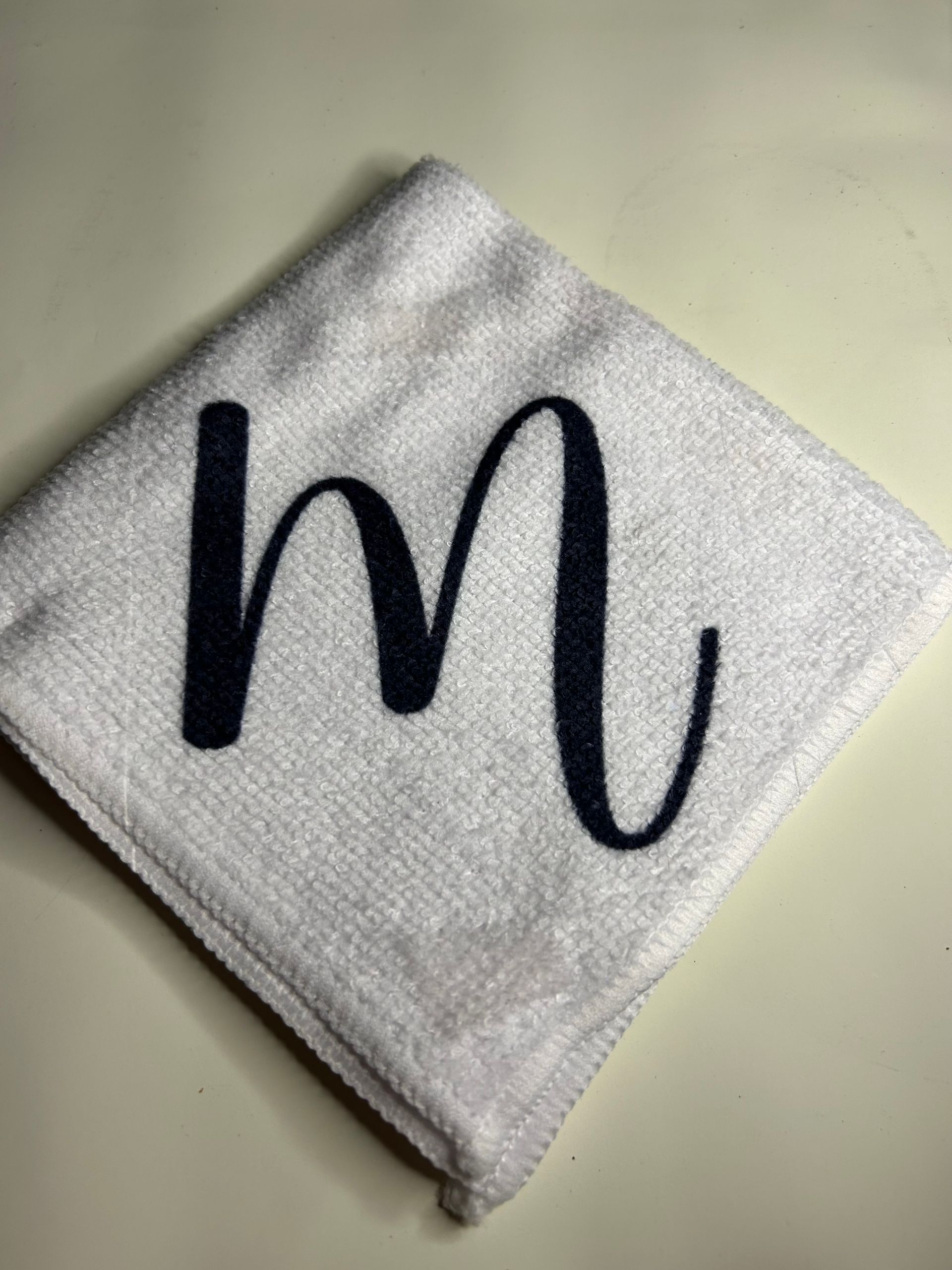 A white towel with the letter m embroidered on it.