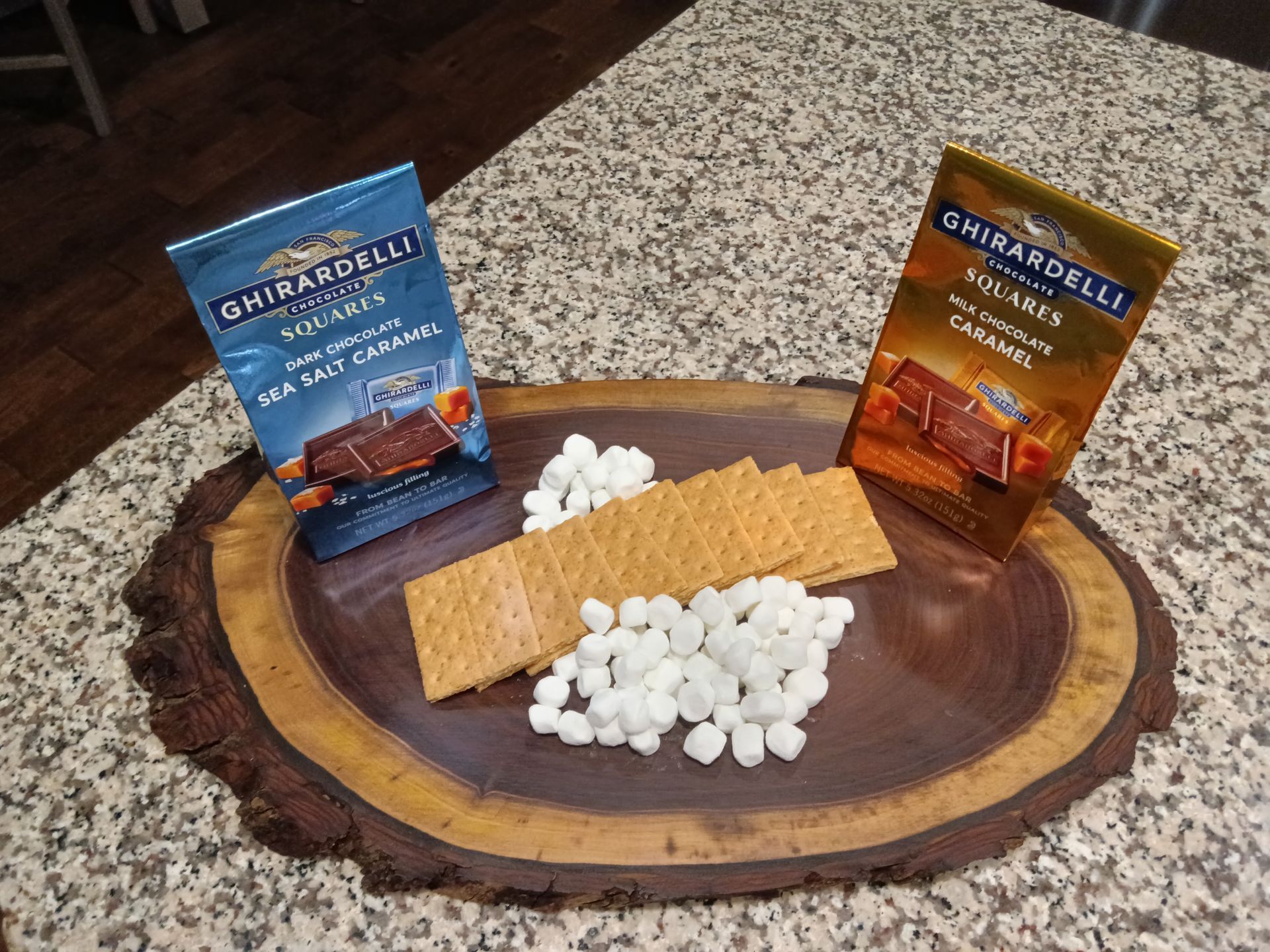 A wooden charcuterie board topped with graham crackers and marshmallows on a counter.