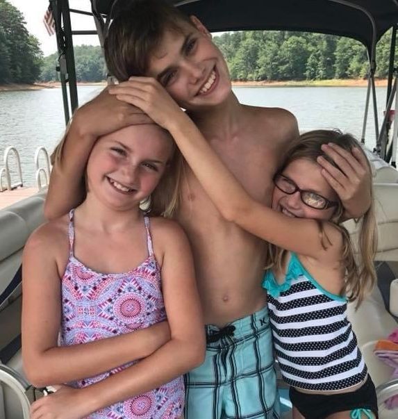 three children hugging each other and smiling on a boat