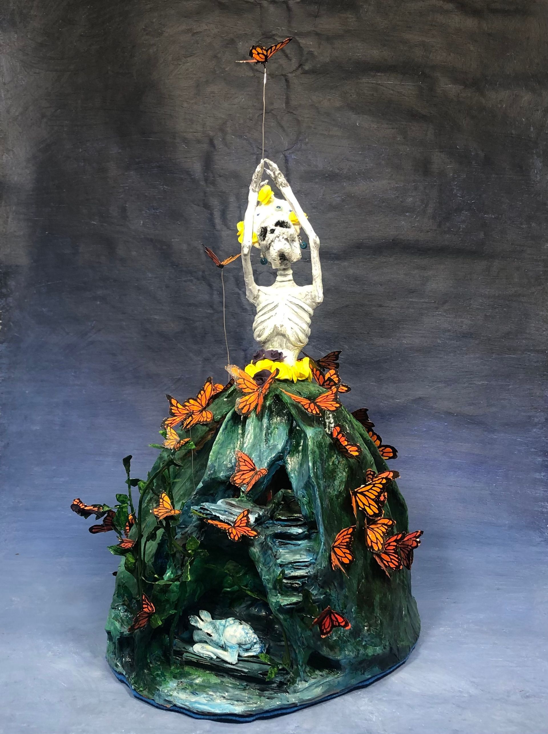 a statue of a skeleton wearing a green dress sitting on top of a rock surrounded by butterflies .