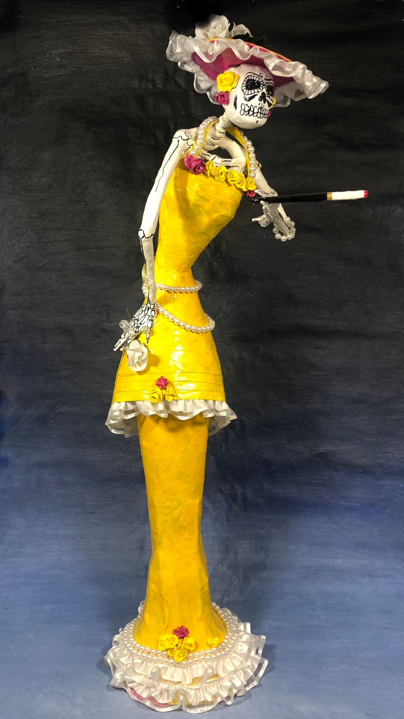 A Skeleton lady wearing a yellow dress with white ruffles and pearls. 