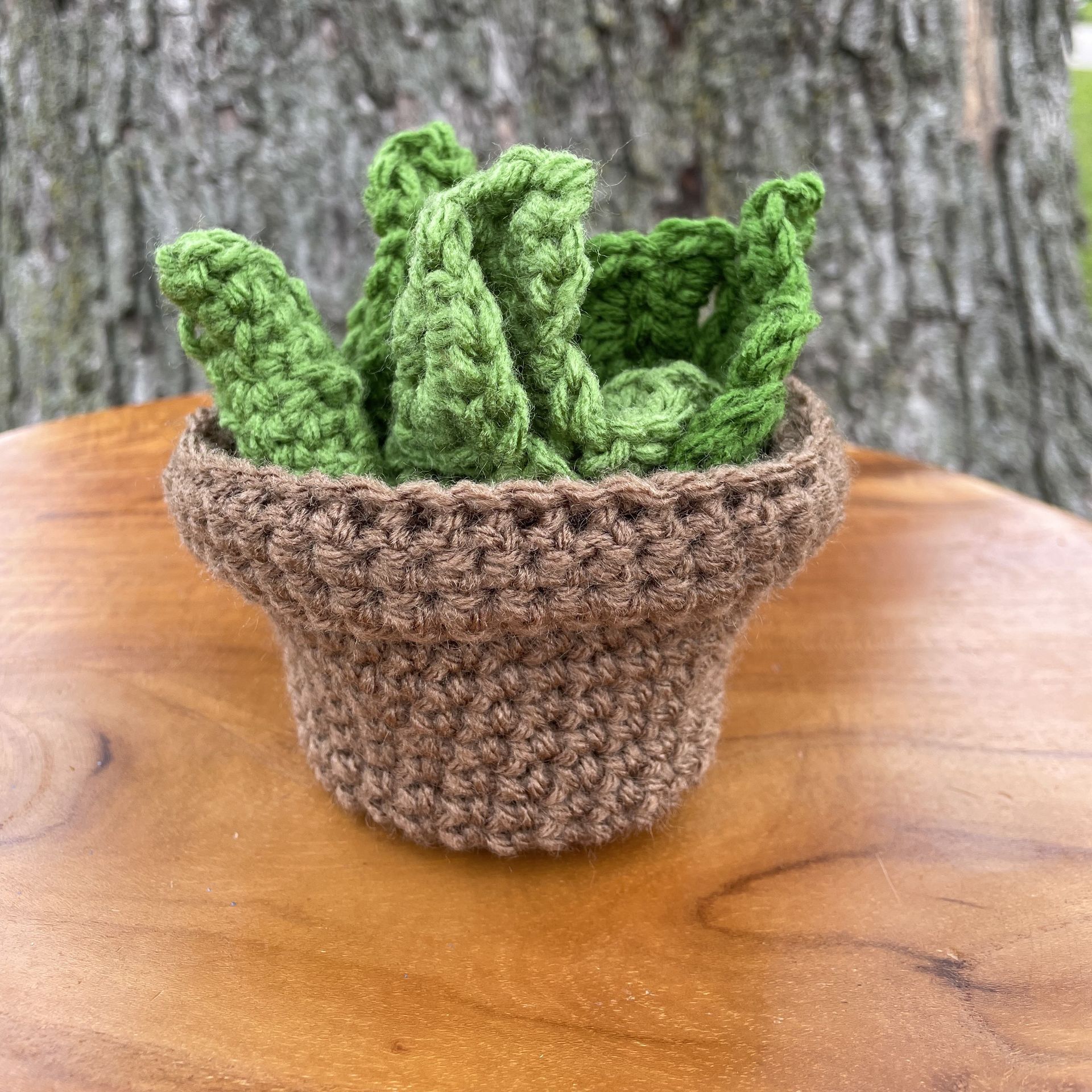 Two green crocheted leaves are sitting on top of a wooden cutting board.