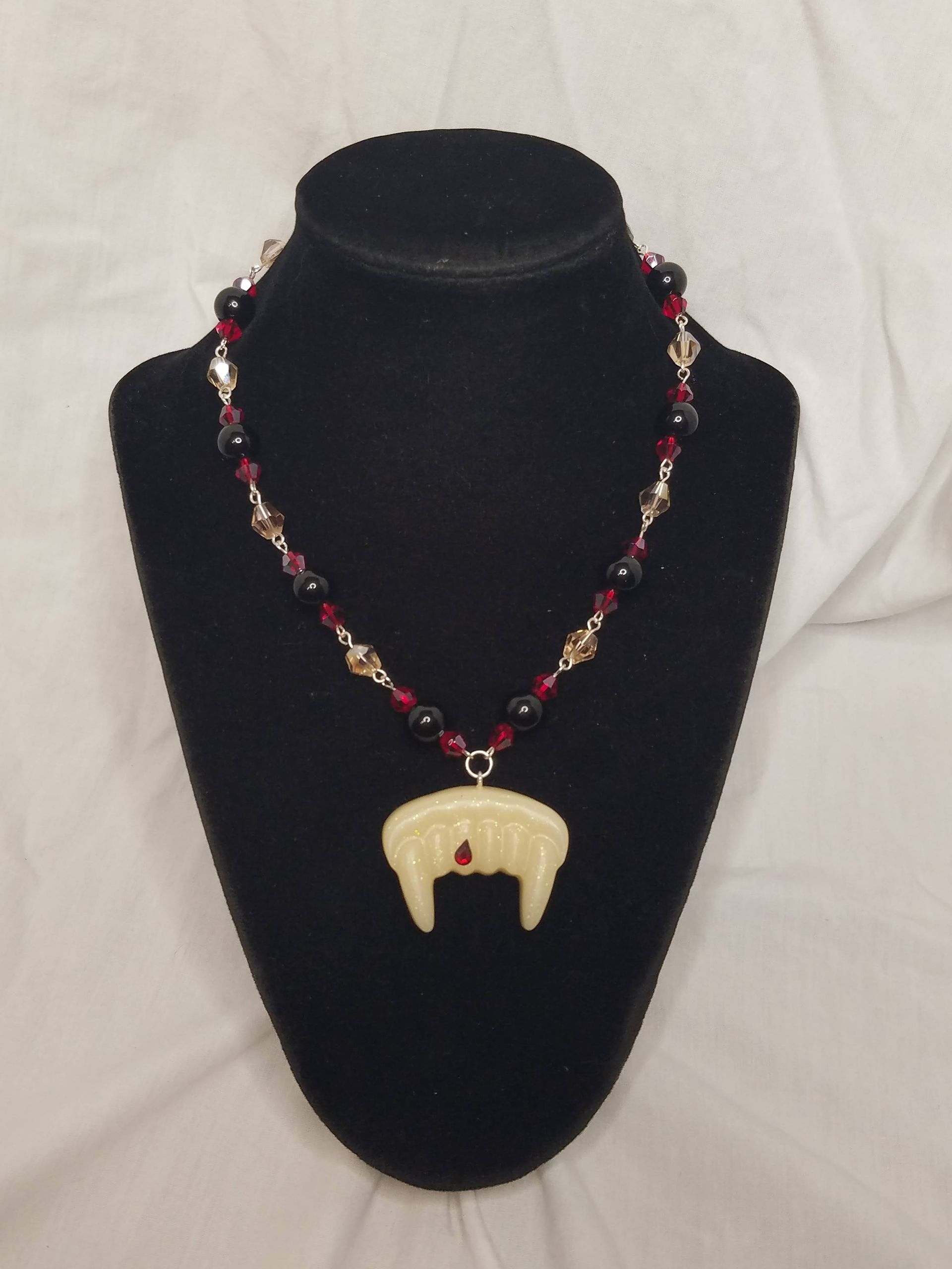 A black mannequin is wearing a necklace with a vampire tooth pendant