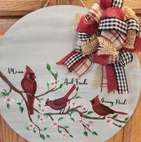 A door sign with three cardinals sitting on a tree branch with flowers. There is a colorful rustic bow.