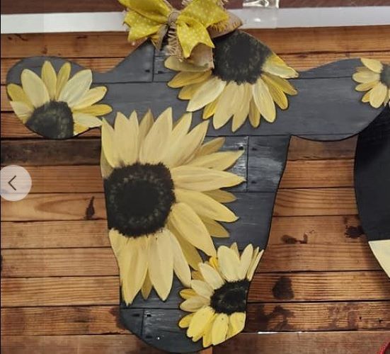 A wooden door sign shaped like a cow head outline with sunflowers on it