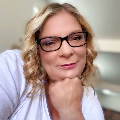 A woman wearing glasses and a white shirt is taking a selfie.