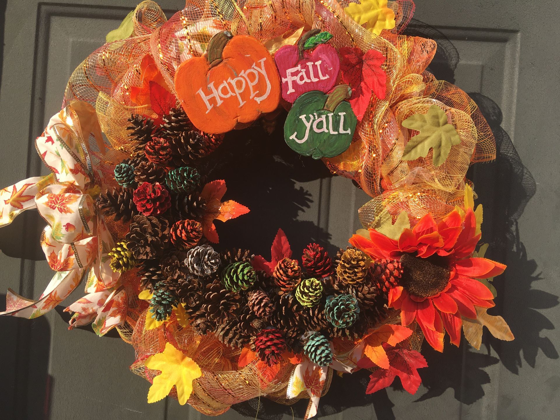 A wreath made from pinecones and ribbon that says happy fall y'all on it