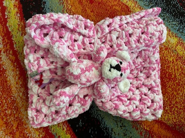 A pink and white crocheted headband with a teddy bear on it.