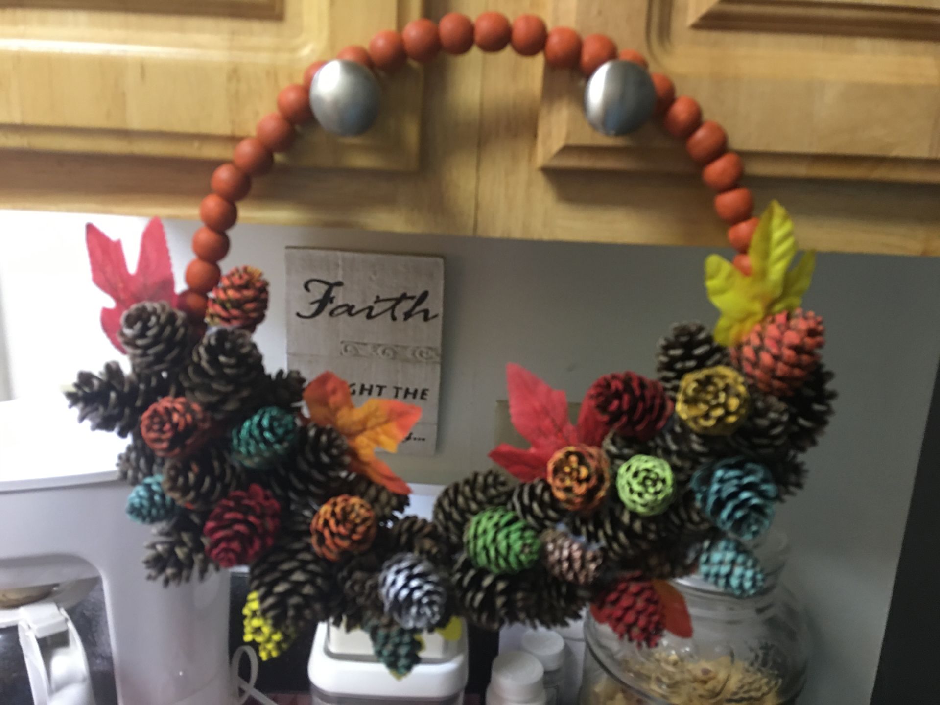 A wreath made of pine cones and beads hangs on a cabinet door
