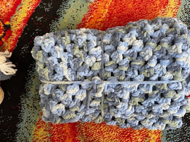A blue and white crocheted scarf is sitting on a colorful rug.