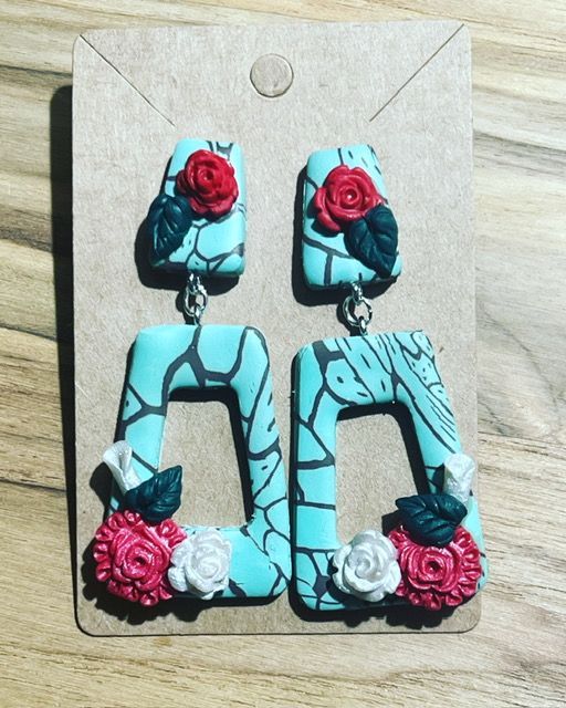 A pair of turquoise earrings with red and white roses