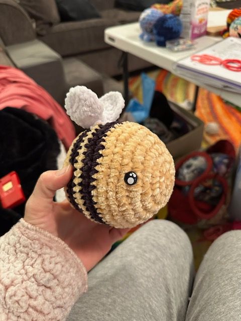 A person is holding a crocheted bee in their hand.