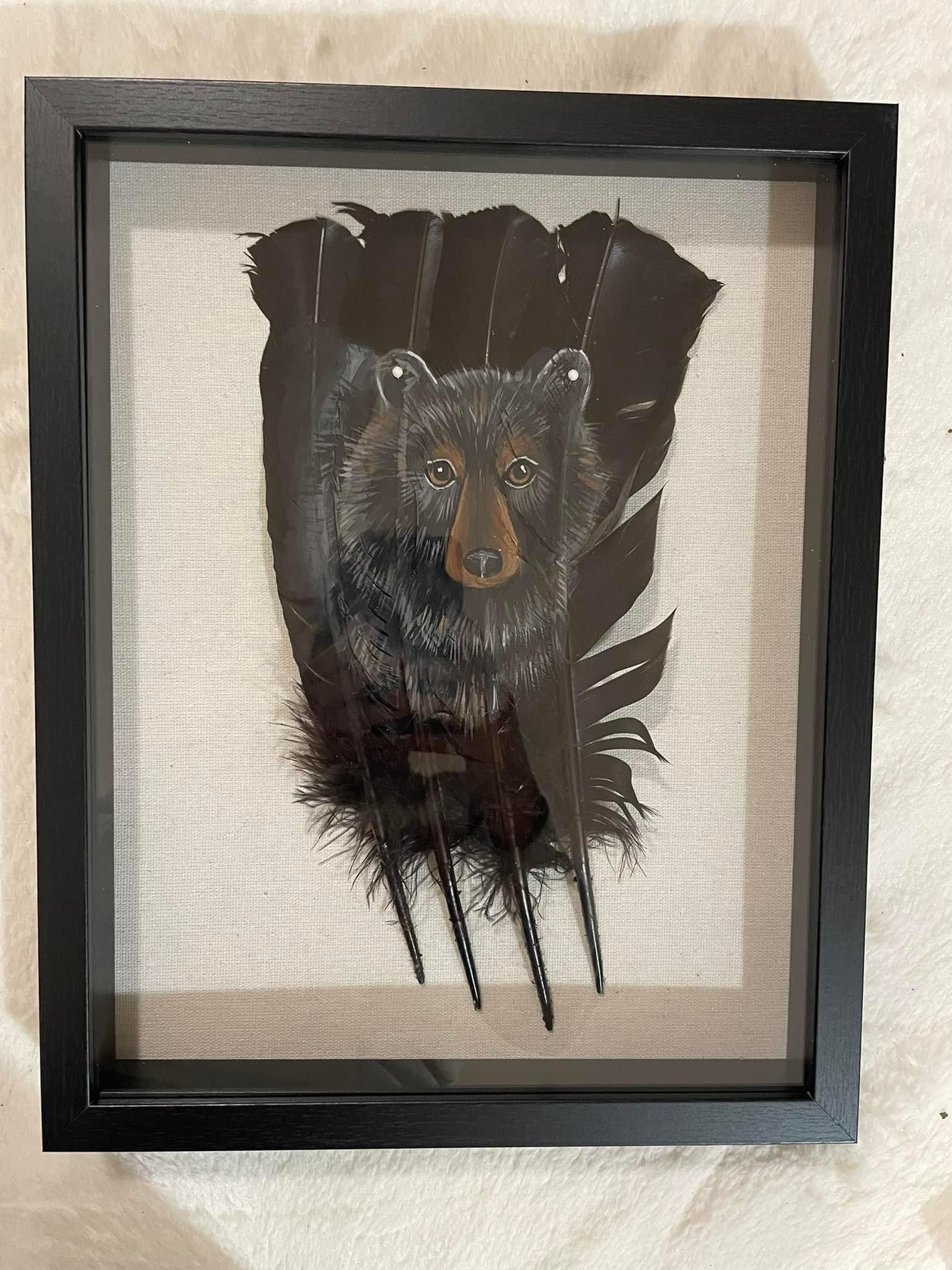 A black bear is sitting on top of a feather in a frame.