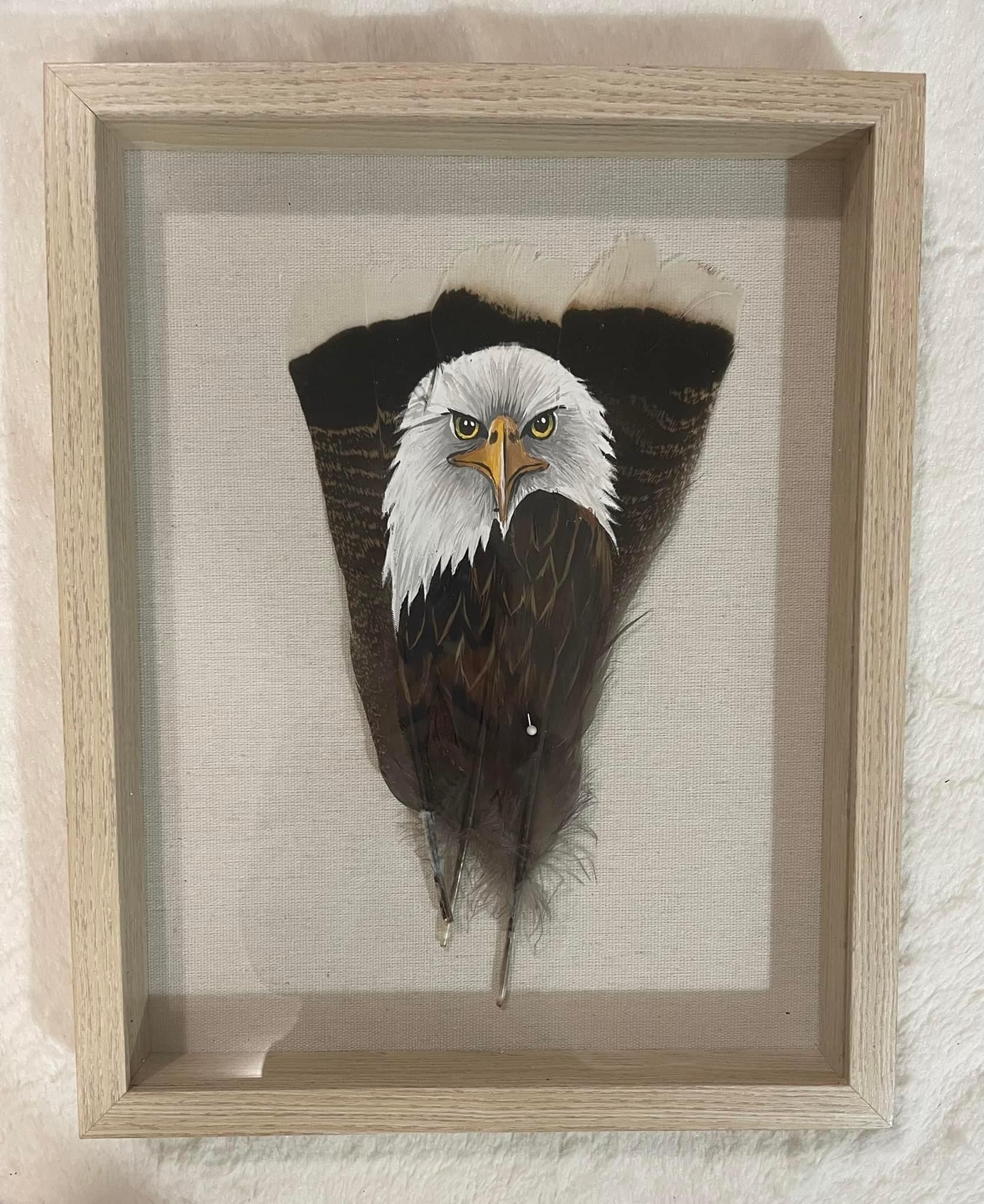 A bald eagle is painted on a feather in a wooden frame.