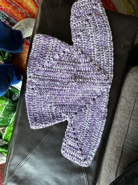 A purple and white crocheted sweater is sitting on a leather couch.