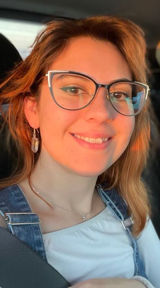 A woman wearing glasses and earrings is smiling in a car.