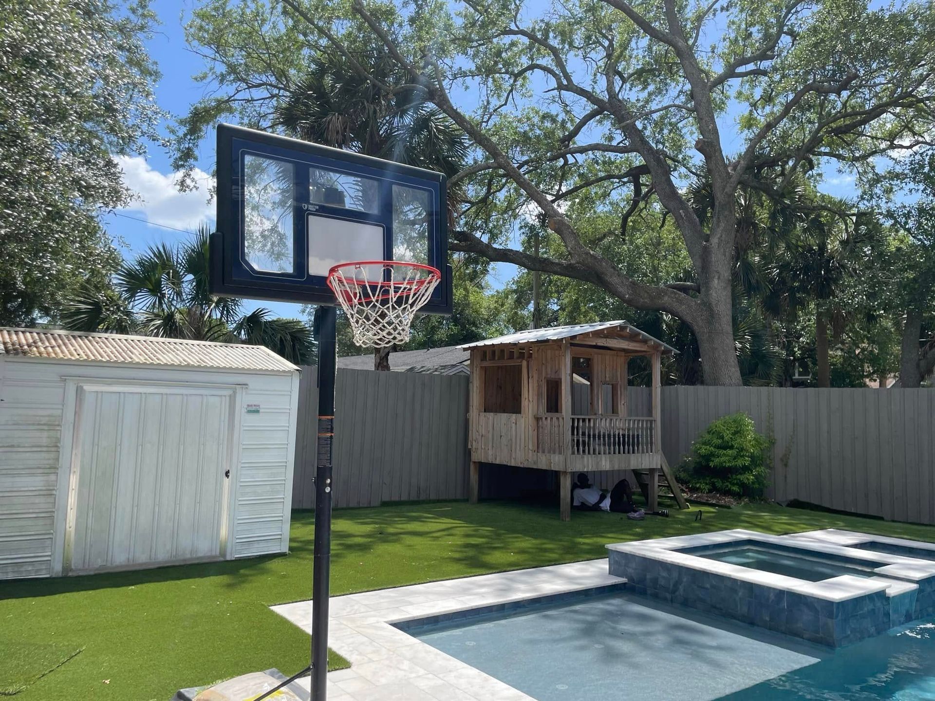 A basketball hoop is sitting next to a pool in a backyard.