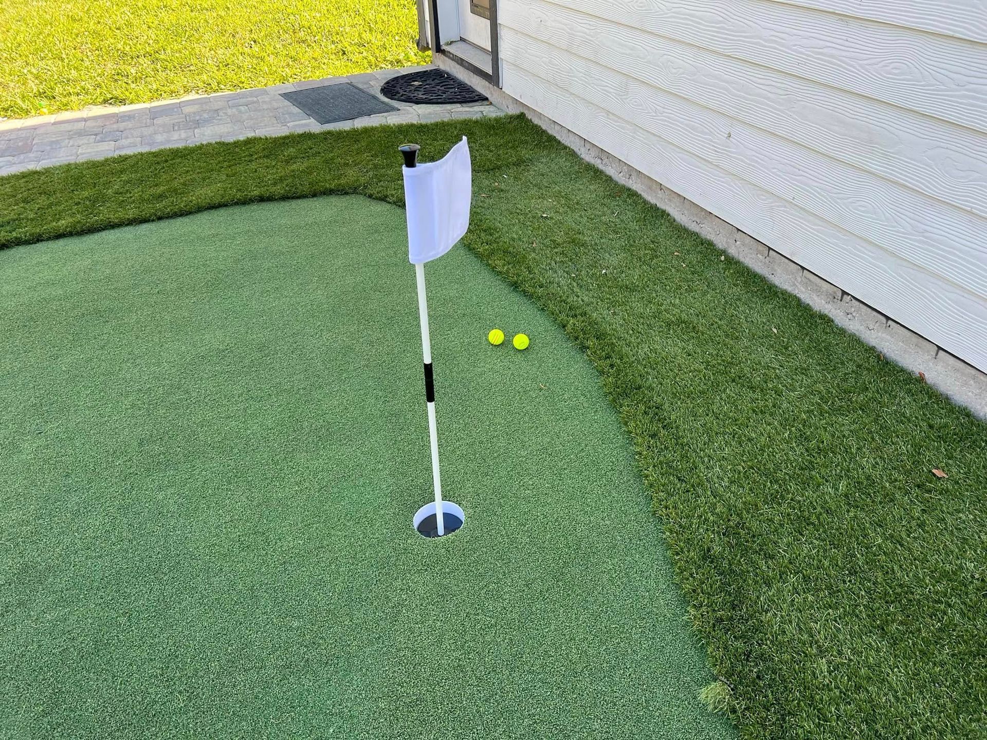 A putting green with a flag and two golf balls in front of a house.